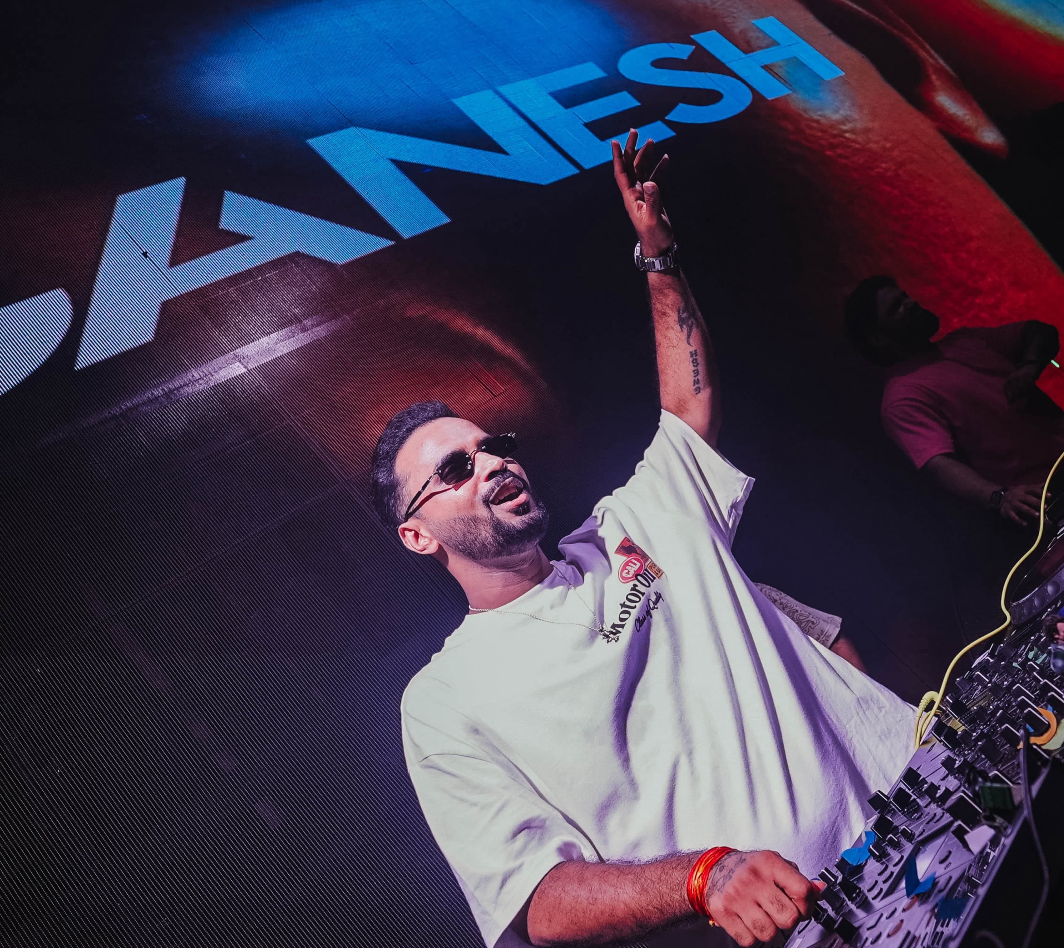 DJ Ganesh performing behind the decks, his name on the screen behind him